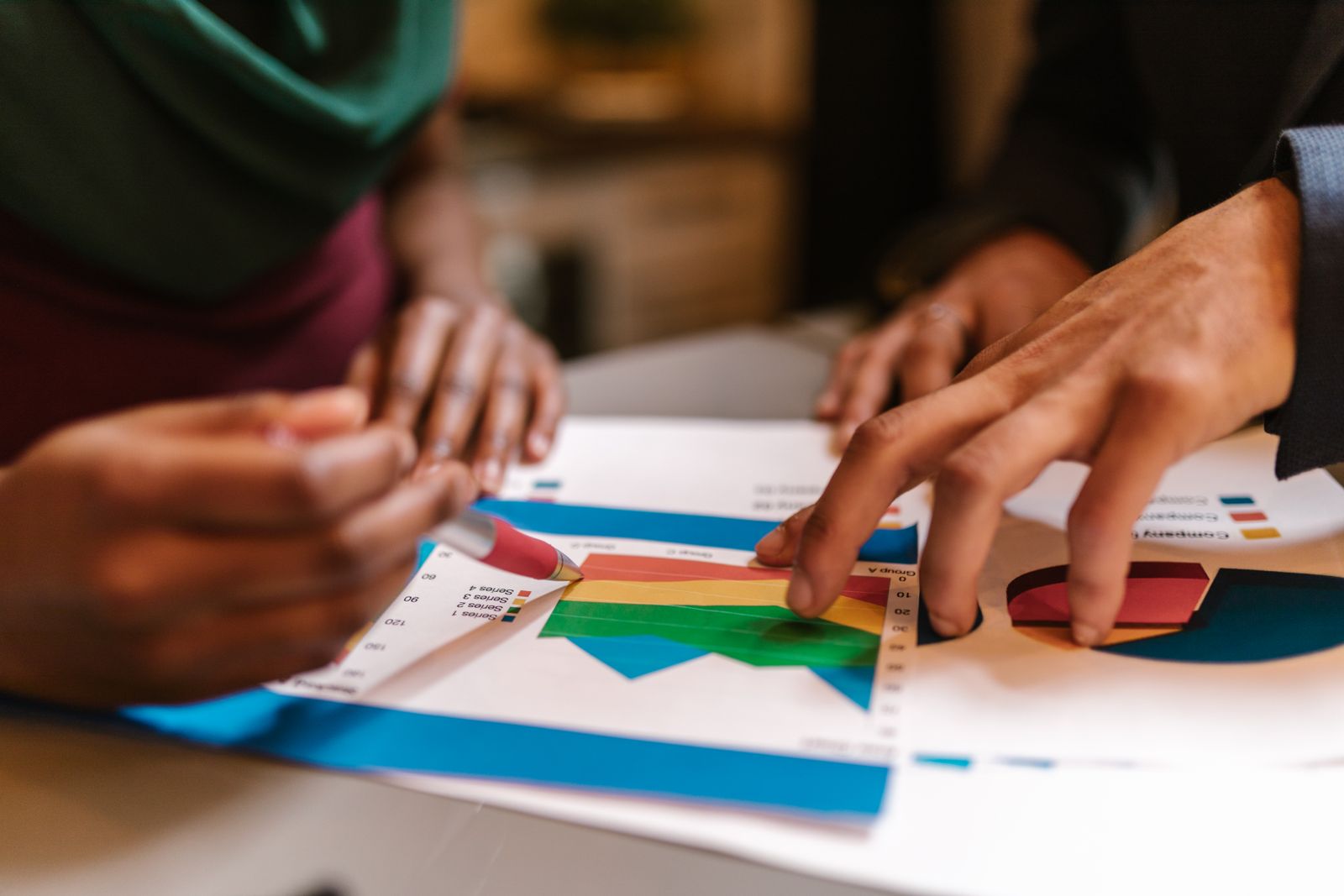 Close-up of hands during a collaborative office meeting analyzing colorful graphs and documents.