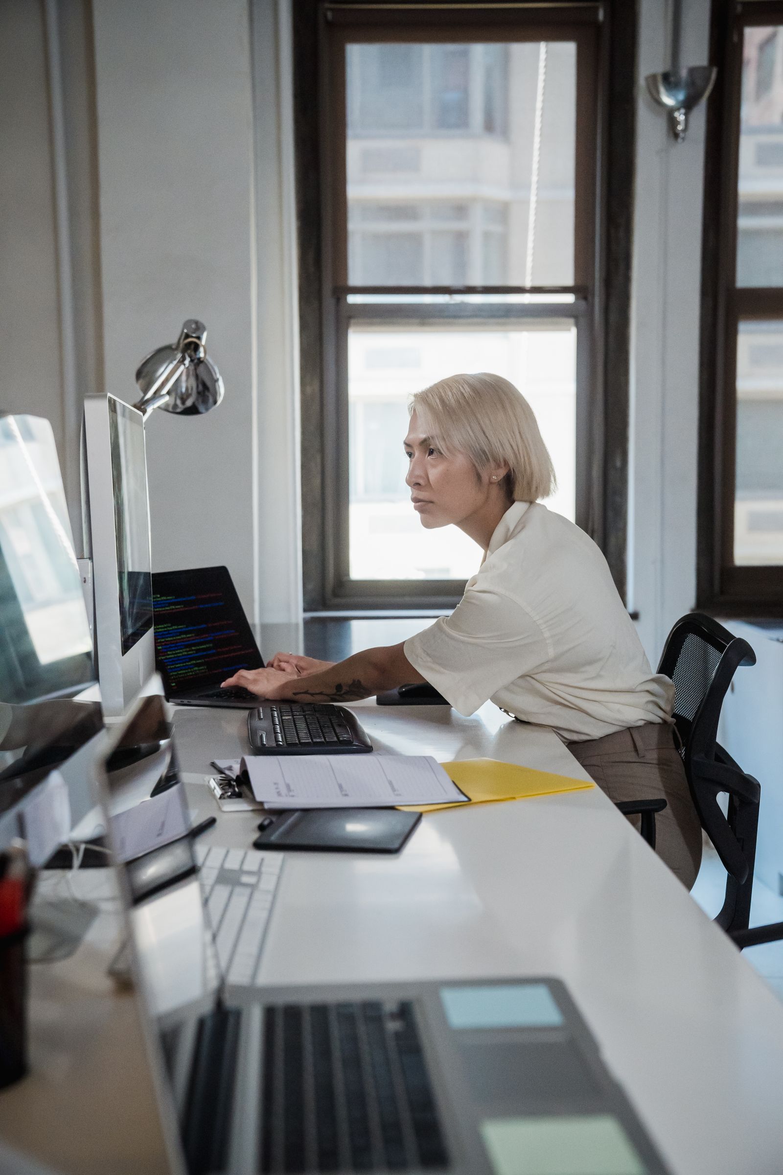 Focused woman working on multiple screens in a modern office setting.