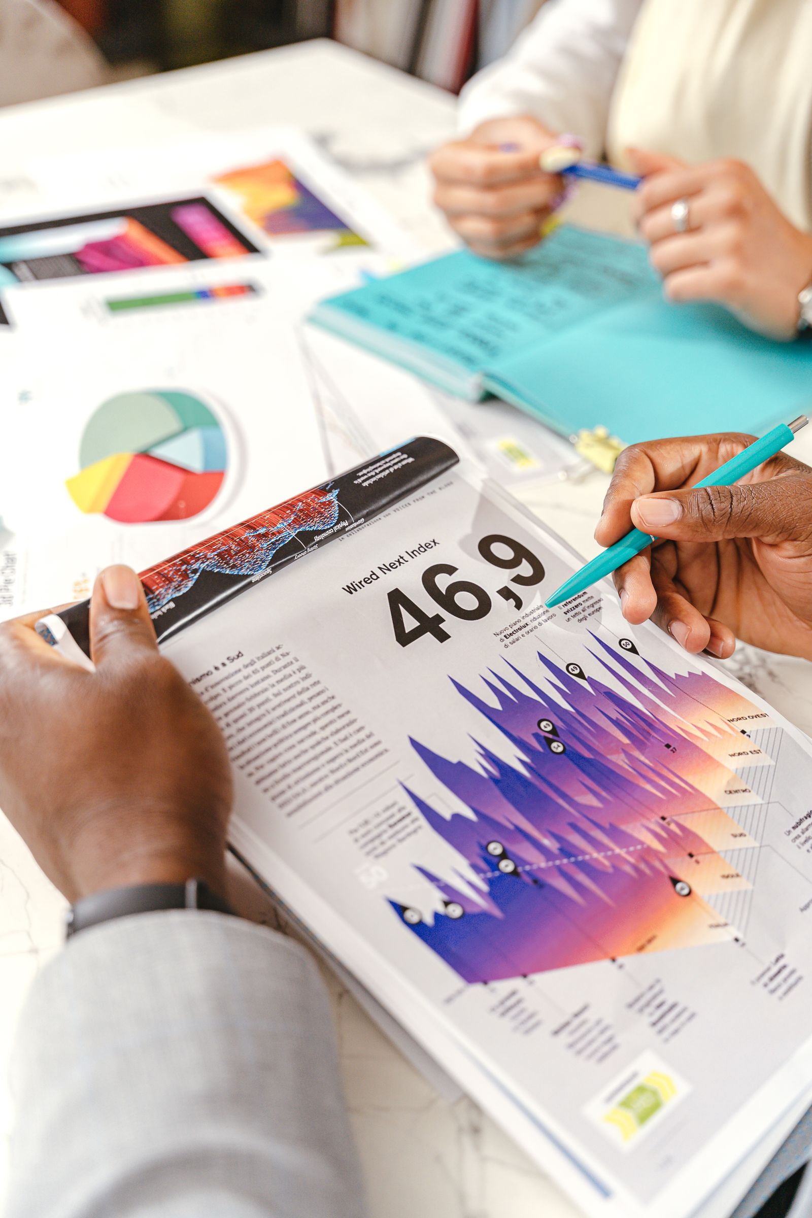 Hands discussing vibrant data charts during a business meeting, with papers and diagrams.